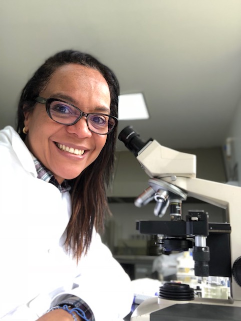 Leyla Rios de Alvarez in a lab coat at a microscope.